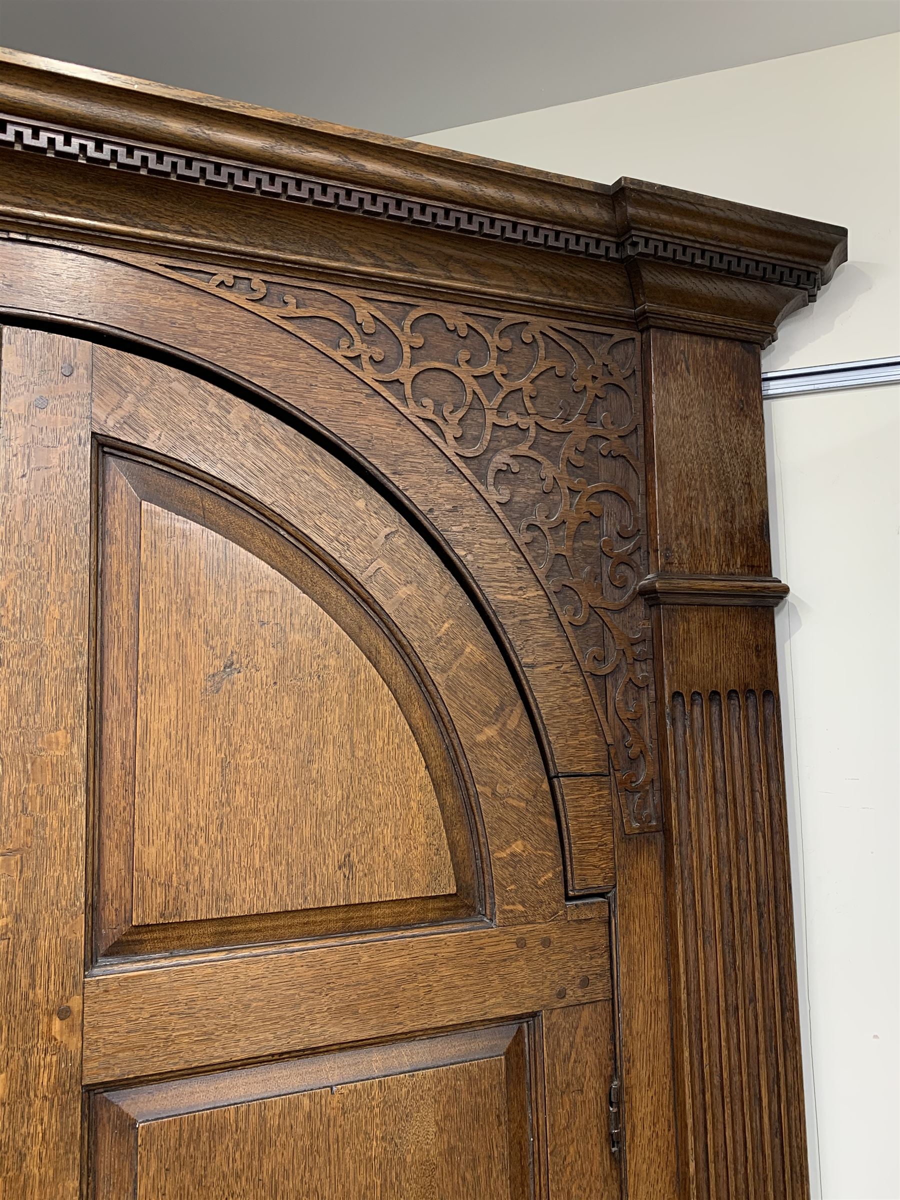 Large George III oak corner cupboard, projecting cornice over two stepped arch doors with fielded panels and blind fret work spandrels, flanked by fluted uprights, cupboard below enclosed by two fielded panel doors, the painted interior fitted with shaped shelves
 