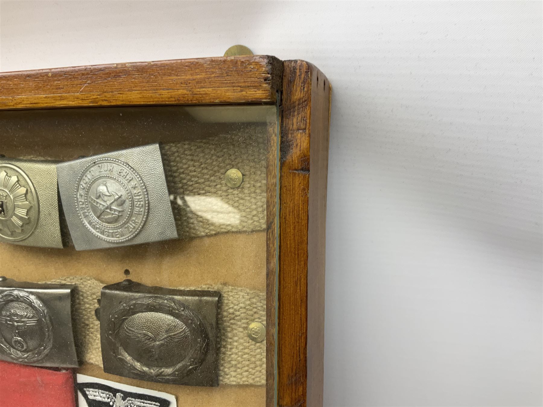 Display of eleven German belt buckles including 'SS', Party Buckle, two Army, Fire Service, two Luftwaffe, NSKK, Hitler Youth and WW1 Army; framed with three cloth badges and an armband