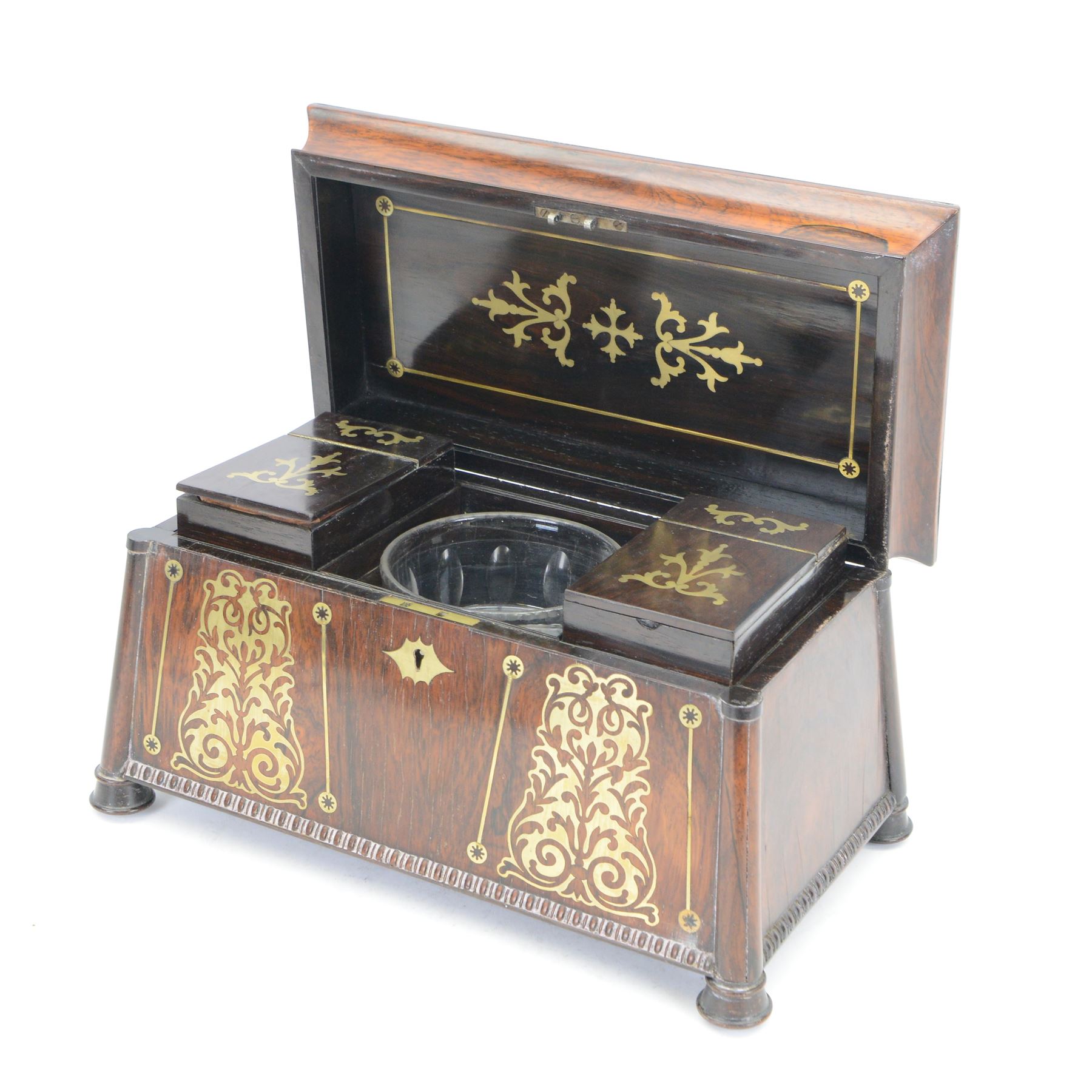 Early 19th century rosewood and brass inlaid tea caddy, of sarcophagus form, the front and hinged opening cover inlaid with brass scrolling panels, opening to reveal a compartmented interior with twin removable boxes with conforming inlaid brass detail to the hinged covers and zinc lining to the interiors, flanking a later glass mixing bowl, the whole upon four turned cylindrical feet, H21cm W36cm D20cm