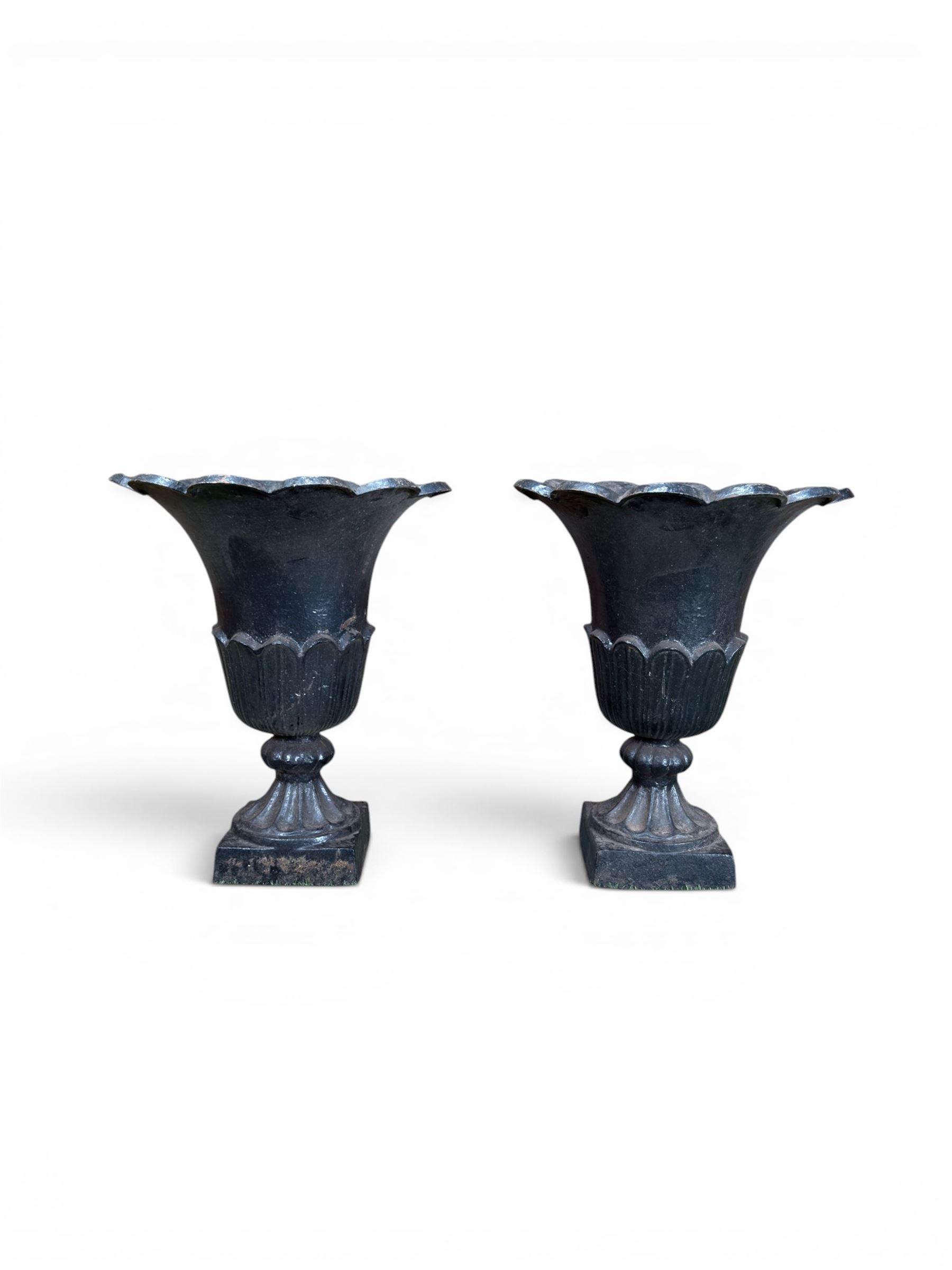 Pair of Victorian large scale cast iron garden urns, flared petal shaped rim with tapering waist, gadrooned base on square plinth, finished in black paint