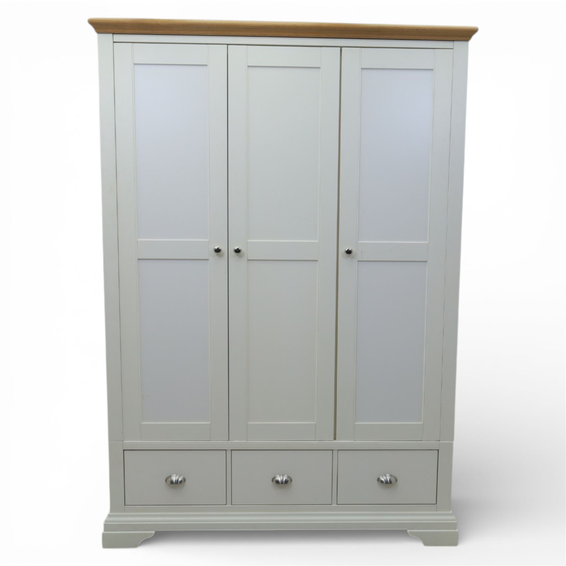 Modern triple wardrobe in white finish with oak moulded top enclosed by three doors with three drawers to base, with metal cup handles raised on bracket feet