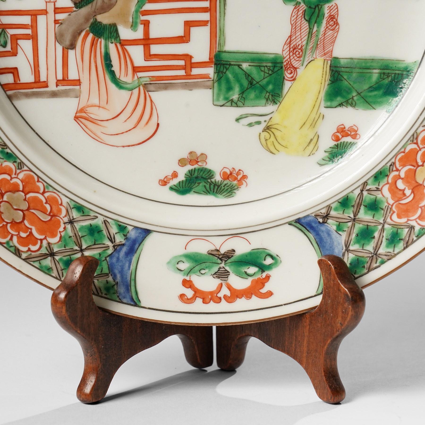 Chinese famille verte plate, painted with two ladies in a garden terrace setting, the border with butterfly and insect vignettes, D23cm 