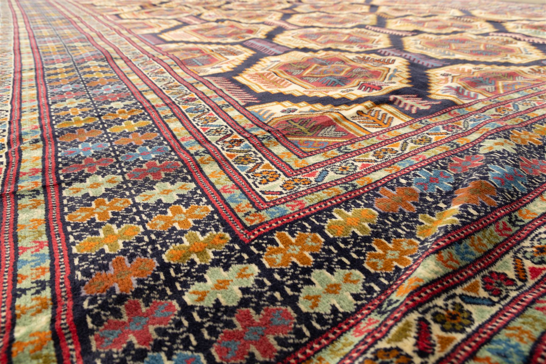 Central Asian Turkmen, main field with octagonal guls enclosing hooked diamond motifs in shades of madder gold, ivory, and indigo set against a dark ground within multiple polychrome borders of geometric devices and stepped motifs 