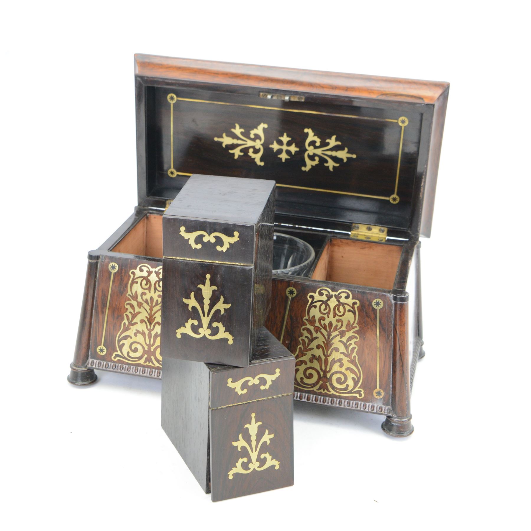Early 19th century rosewood and brass inlaid tea caddy, of sarcophagus form, the front and hinged opening cover inlaid with brass scrolling panels, opening to reveal a compartmented interior with twin removable boxes with conforming inlaid brass detail to the hinged covers and zinc lining to the interiors, flanking a later glass mixing bowl, the whole upon four turned cylindrical feet, H21cm W36cm D20cm