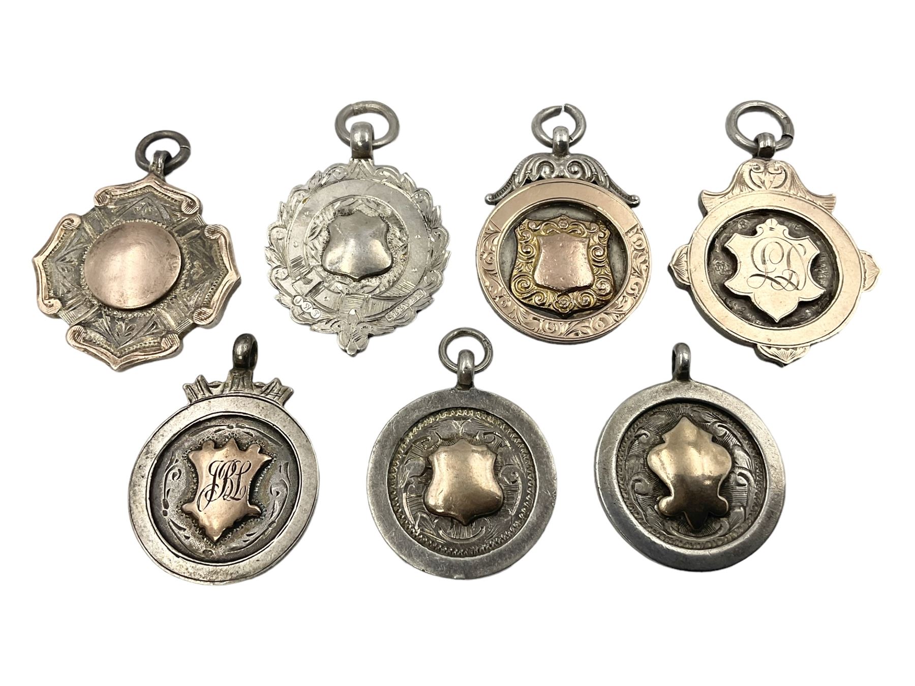 Seven early 20th century silver gold faced cartouche fobs, to include a circular example, with rose gold border and cartouche within an embossed yellow gold border, engraved verso, and a double sided example, all hallmarked with various dates and makers

