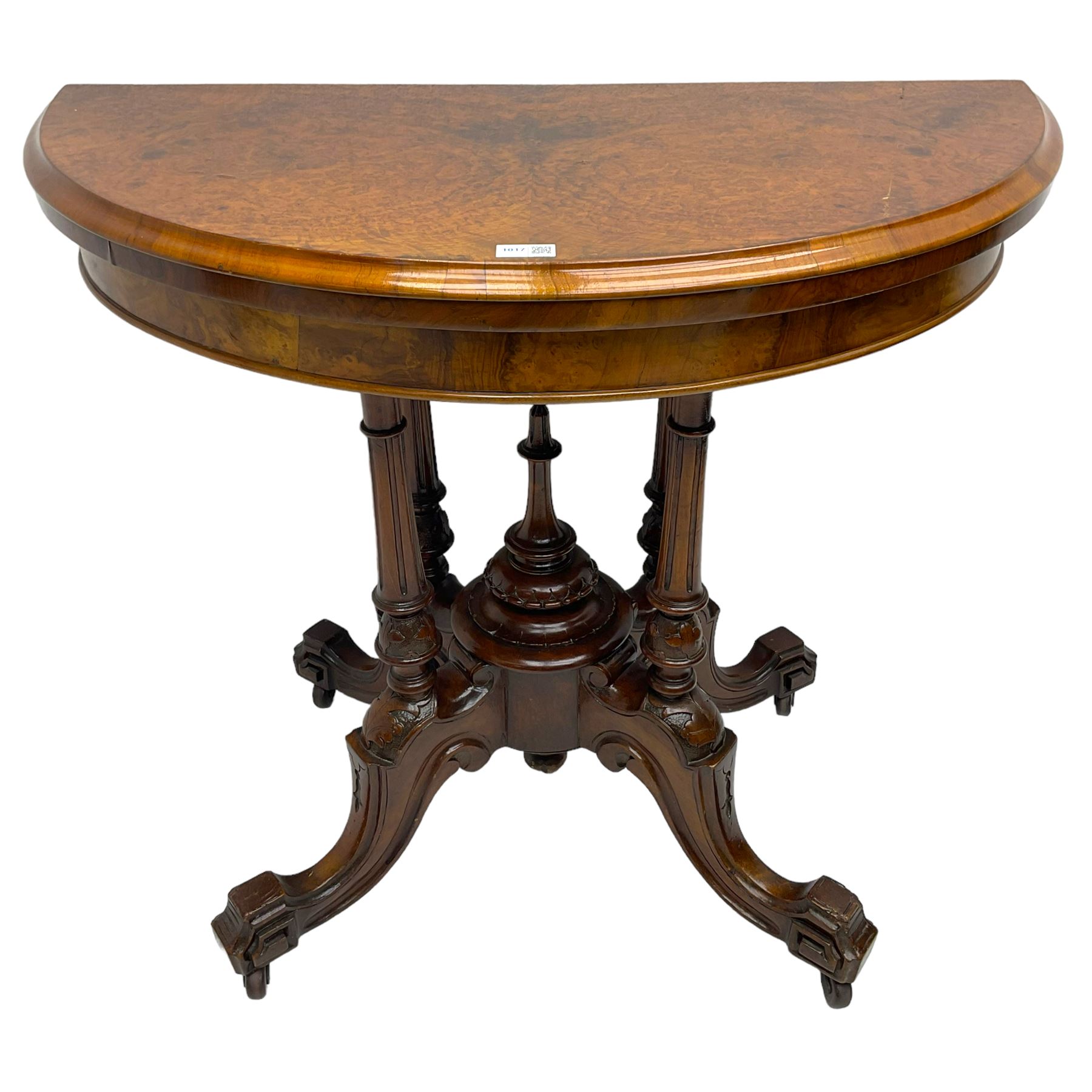 Victorian figured walnut demi-dune card table, the fold-over moulded top with circular baize lining, on four turned pillars with central finial platform, four splayed moulded supports with angular scrolled feet, on castors