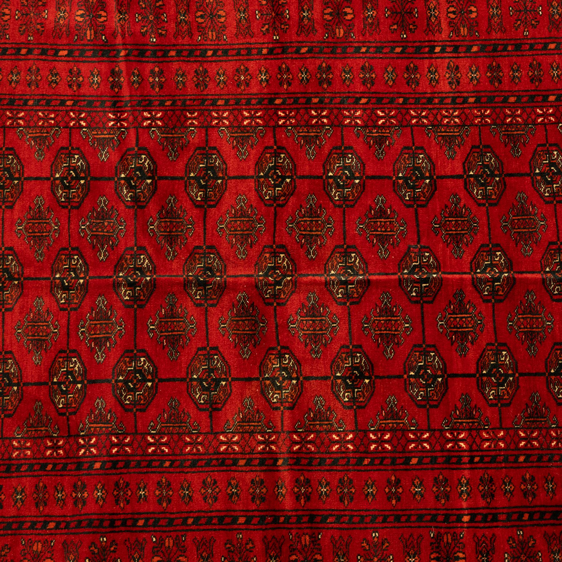 Turkman hand-knotted carpet, deep red ground, with an all-over field of repeating gul motifs arranged in rows, enclosed by multiple red geometric borders with stylised flowerheads and hooked motifs, flanked by narrow patterned guard stripes, with wool fringes