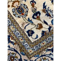 Persian Kashan ivory ground rug, the field decorated with stylised plant motifs and interlacing leafy branches, scrolling border decorated with further plant motifs, floral design guard bands  