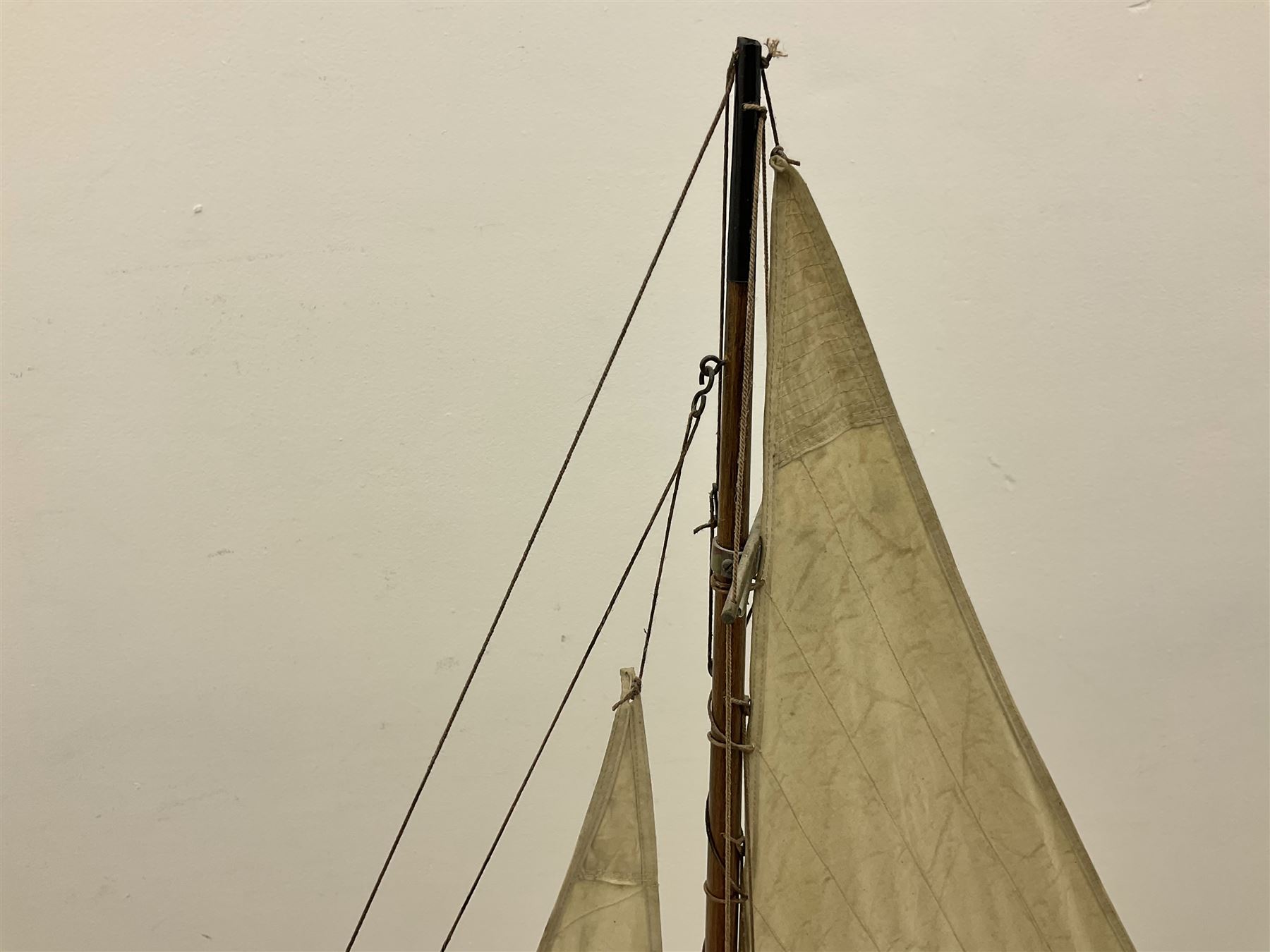 Early 20th century large pond yacht with mahogany hull, stained pine keel with brass rudder, simulated deck hatches and brass fittings, rigged as a staysail schooner (?) with four sails L117cm H148cm; loose mounted on stained pine stand