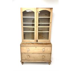 19th century stripped pine cabinet on chest, two glazed cupboard doors enclosing three adjustable shelves, two long drawers on the base unit, turned supports 