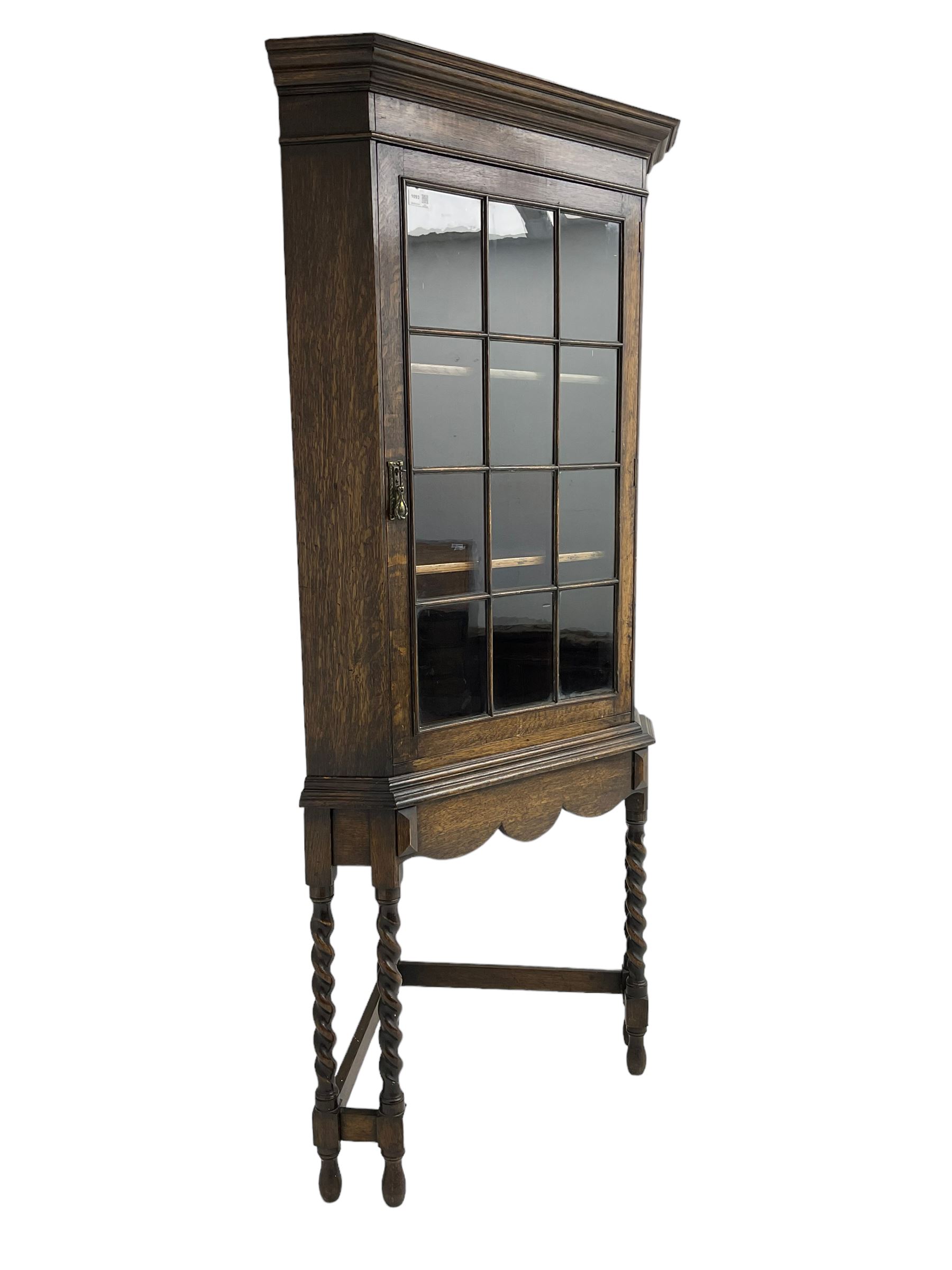Early to mid-20th century oak corner display cabinet, projecting cornice over astragal glazed door, on spiral turned supports joined by stretchers