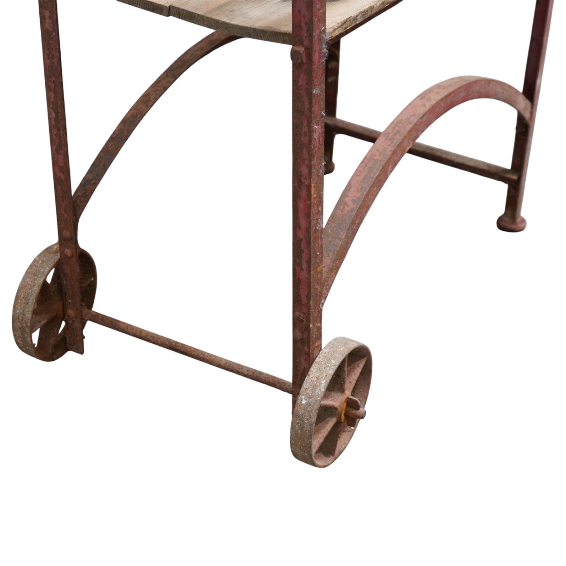 Cast iron and wooden saddle rack, arch form with shelf beneath and wheels to one end, pair of shaped handle poles