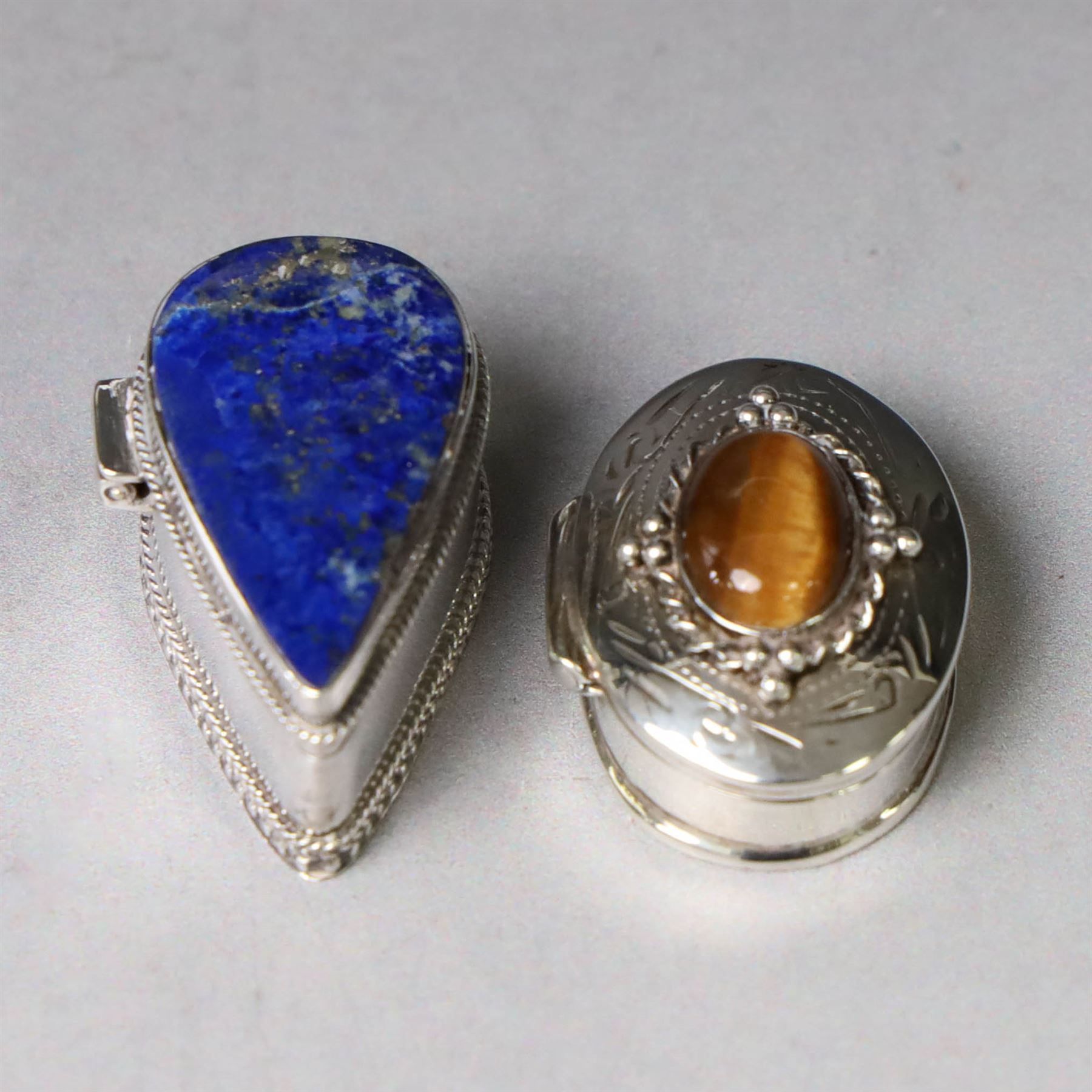 Two modern silver pill boxes, the first example of oval form, the hinged cover set with a tigers eye cabochon with beaded mount, and engraved scroll edge, hallmarked NC, London import 1995, W3cm, the second of teardrop form, the hinged cover set with lapis lazuli, marked 925, L3.5cm