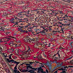 North East Persian Mashad hand-knotted carpet, rich madder red field with central cusped foliate medallion with issuing scrolling arabesques, palmettes, and floral sprays, enclosed within a broad indigo main border of bold palmettes, between multiple guard stripes, with cotton fringe ends 