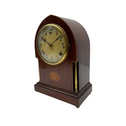 A late 19th century American  mantle clock in a “Lancet” case manufactured by the  Gilbert Clock Factory, Connecticut,  mahogany veneered case with an oval inlay, satinwood stringing to the edge and two recessed brass pillars, on a moulded plinth with four bun feet, enamel dial with upright Arabic numerals and spade hands, fast/slow regulation, with a convex glass and spun brass bezel, eight-day movement striking the hours and half hours on a coiled gong. No pendulum.