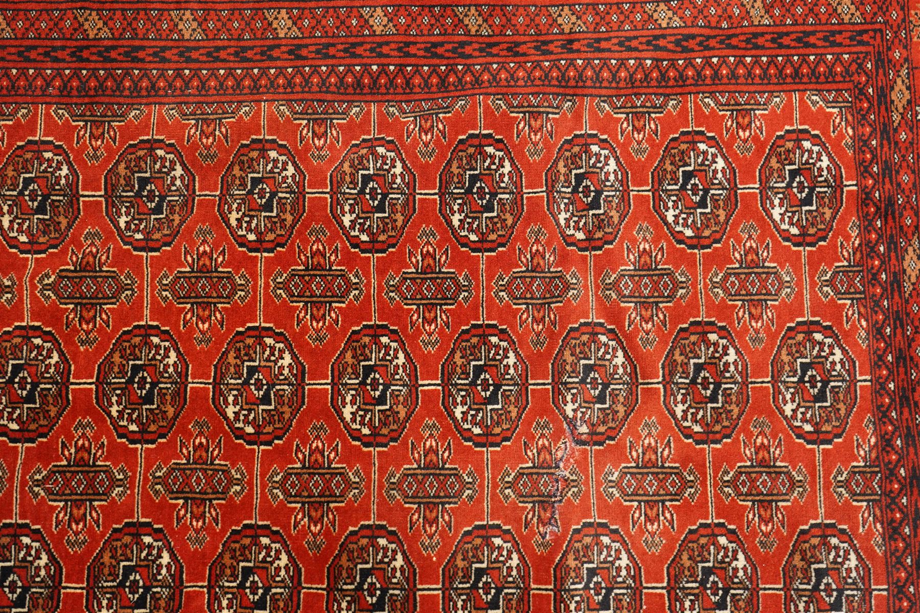 Turkmen hand-knotted carpet, madder red field, with an all-over design of row of Tekke guls, each enclosing stylized cruciform and geometric devices in tones of ivory, dark brown, and indigo, principal border of stylized geometric motifs, flanked by guard border with angular latch hook geometric designs, with cotton fringe ends 