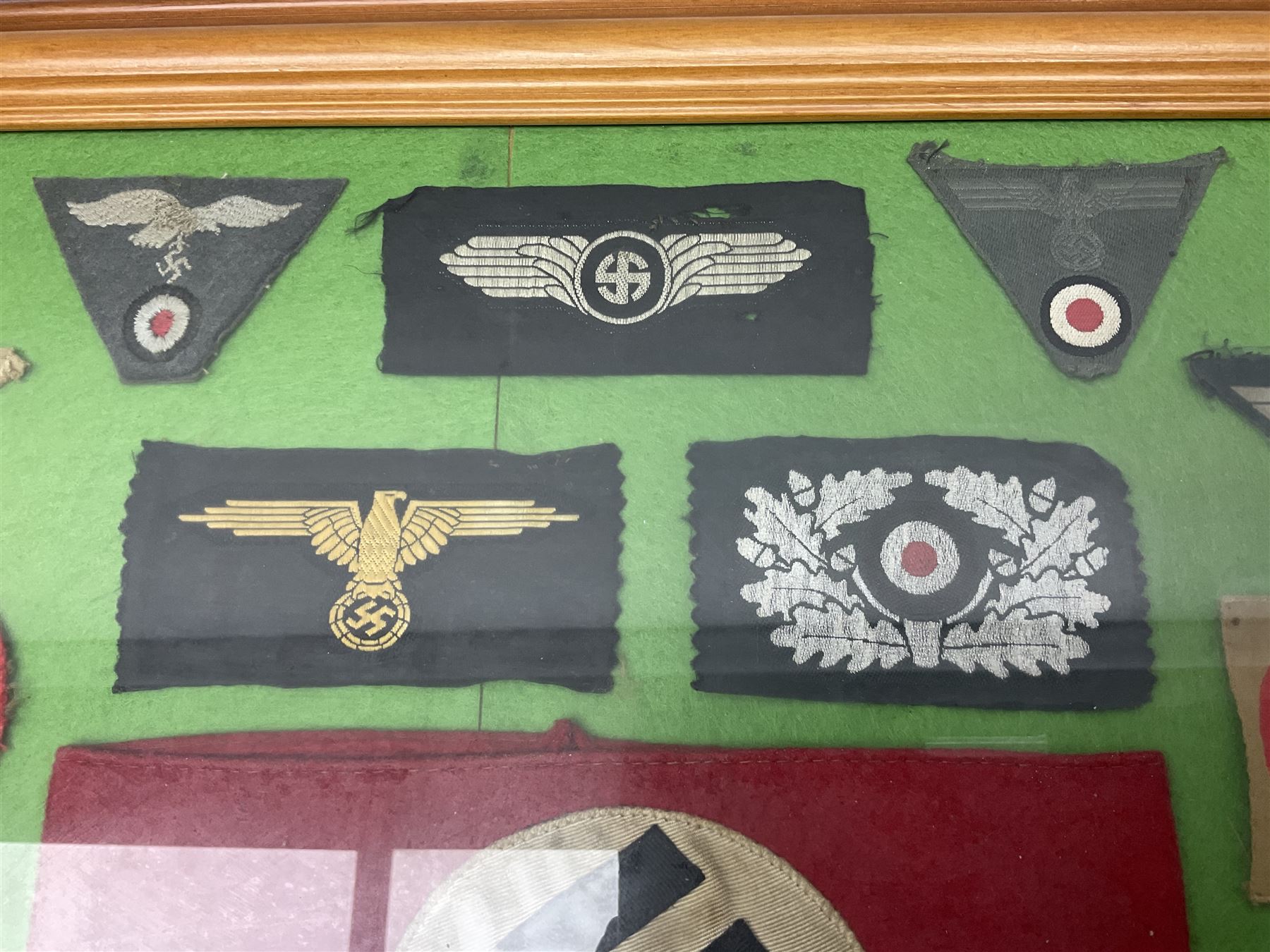 Framed display of thirty-four WWII German cloth badges including Luftwaffe pilot, Paratrooper, Afrikakorps cuff title, sleeve insignia for 'SS' Foreign Volunteers, various breast eagles including Luftwaffe, Army etc, RAD badges, Party Armband, rank and trade insignia, cap insignia etc; 40 x 50cm in modern pine frame