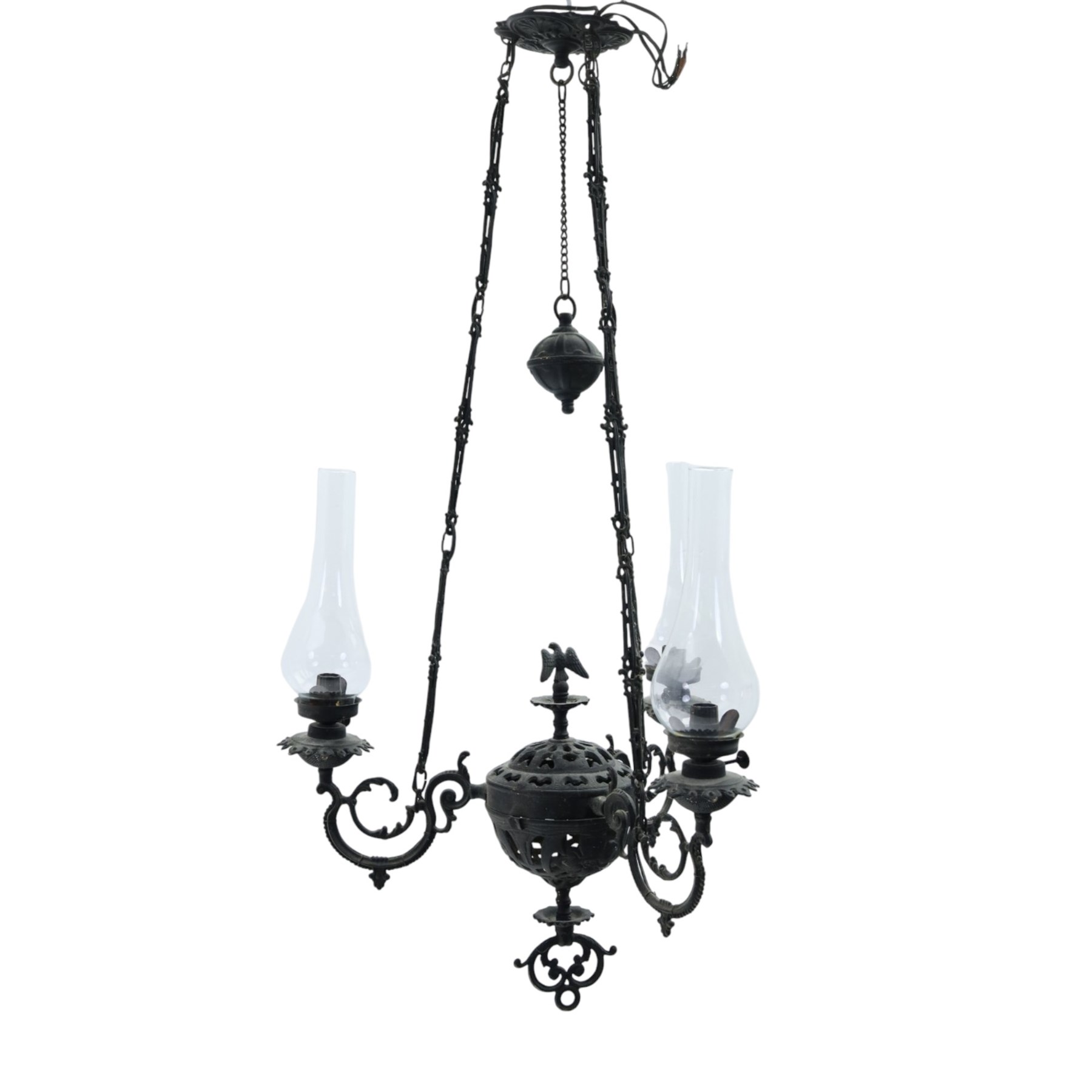 Late 19th century wrought metal hanging ceiling lamp, the ornate pierced central reservoir-form body with mounted eagle, three scrolling branches fitted with three clear glass chimney shades, suspended by decorative chains from a pierced ceiling rose