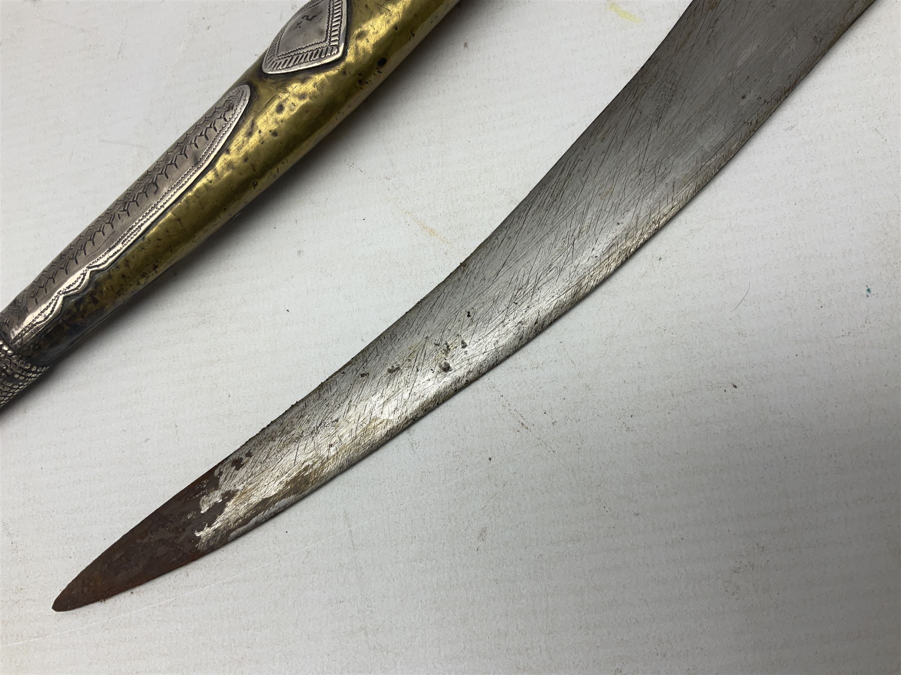 Late 19th/20th century Middle Eastern jambiya dagger the 36cm broad curved double edged steel blade with traces of script, horn and copper backed waisted white metal hilt with three roundel buttons; in ornate white metal and leather mounted brass and steel scabbard L60.5cm overall