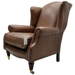 Georgian design wingback armchair, upholstered in brown leather with stud band and piping, turned and fluted front feet on brass cups and castors