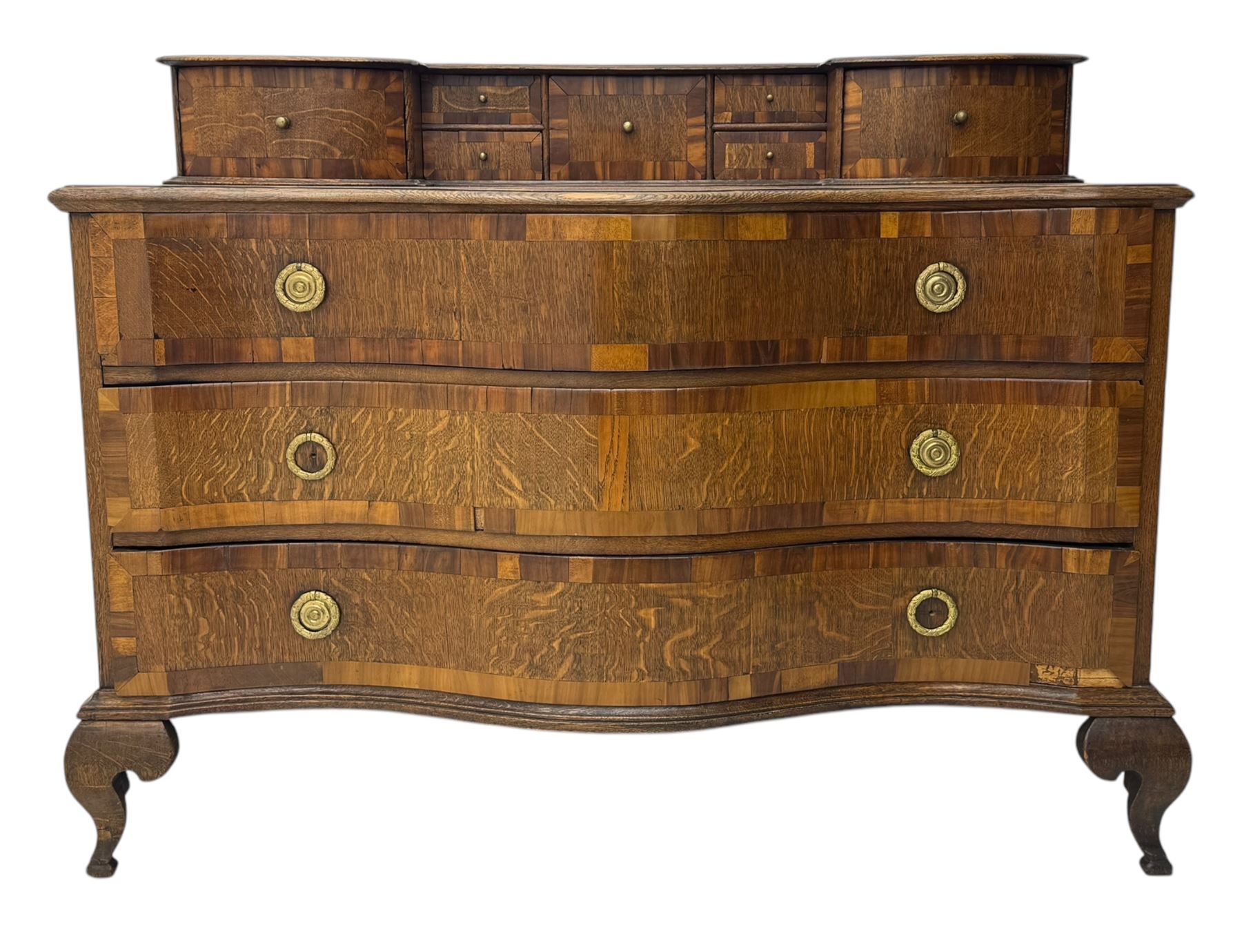 Late 19th century continental oak commode, serpentine fronted with parquetry and crossbanded decoration, the raised superstructure back fitted with a central bank of five recessed drawers flanked by concave drawers, above three full-width drawers with brass ring handles, raised on cabriole supports