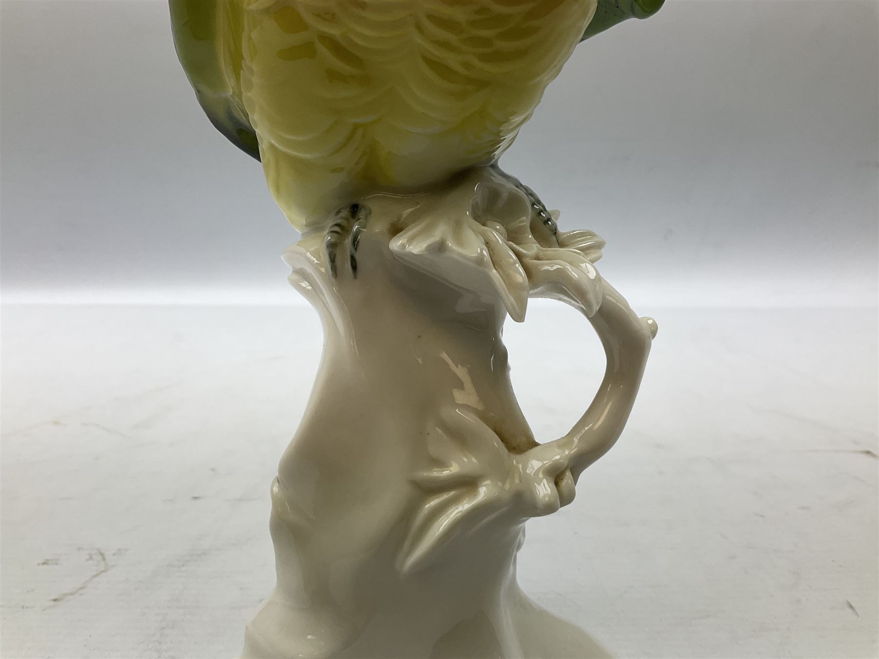 Karl Ens porcelain figure of a parrot, modelled with yellow breast, blue back and wings and green tail, perched upon on a blossoming branch, with blue printed factory mark beneath, H24.5cm