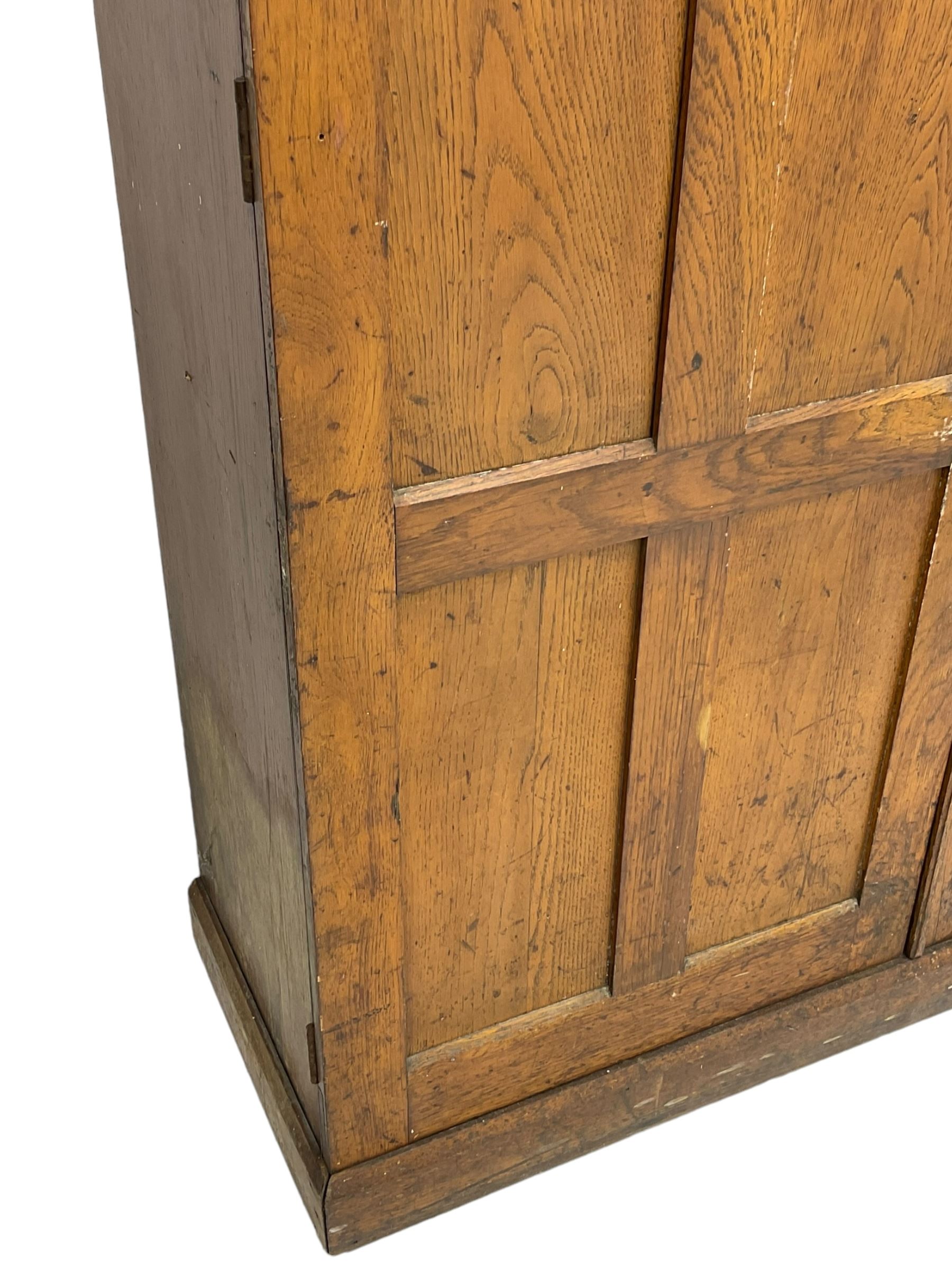 The North of England School Furnishing Company Limited Darlington - early 20th century oak school cupboard, projecting moulded cornice over two panelled doors, fitted with shelves, on chamfered plinth base 