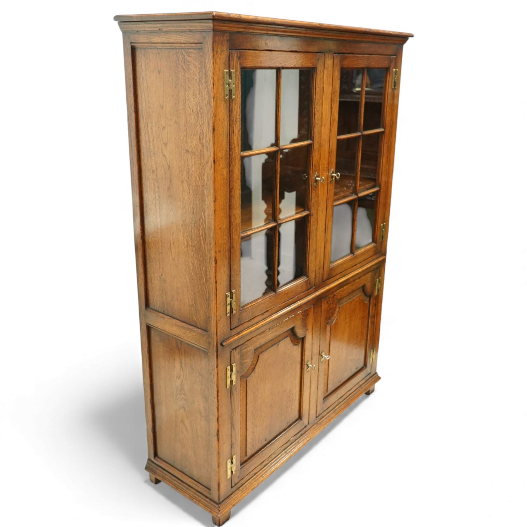 Late 20th century oak cabinet in the manner of Titchmarsh & Goodwin, rectangular top over a pair of nine-pane glazed doors enclosing adjustable shelves, above two moulded panel cupboard doors, raised on block feet