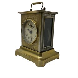 A German Juhngans “Joker” carriage clock with a musical alarm c1890, with a circular card dial with roman numerals, minute track and subsidiary alarm dial, brass case with carrying handle and foliate decoration to the front, wound and set from the rear. With key.

