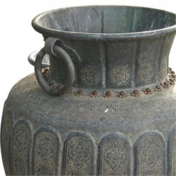 Pair of large Indian cast metal garden urns, each of bulbous form with engraved foliate and script panels, twin ring handles to the neck, raised on fluted pedestal bases