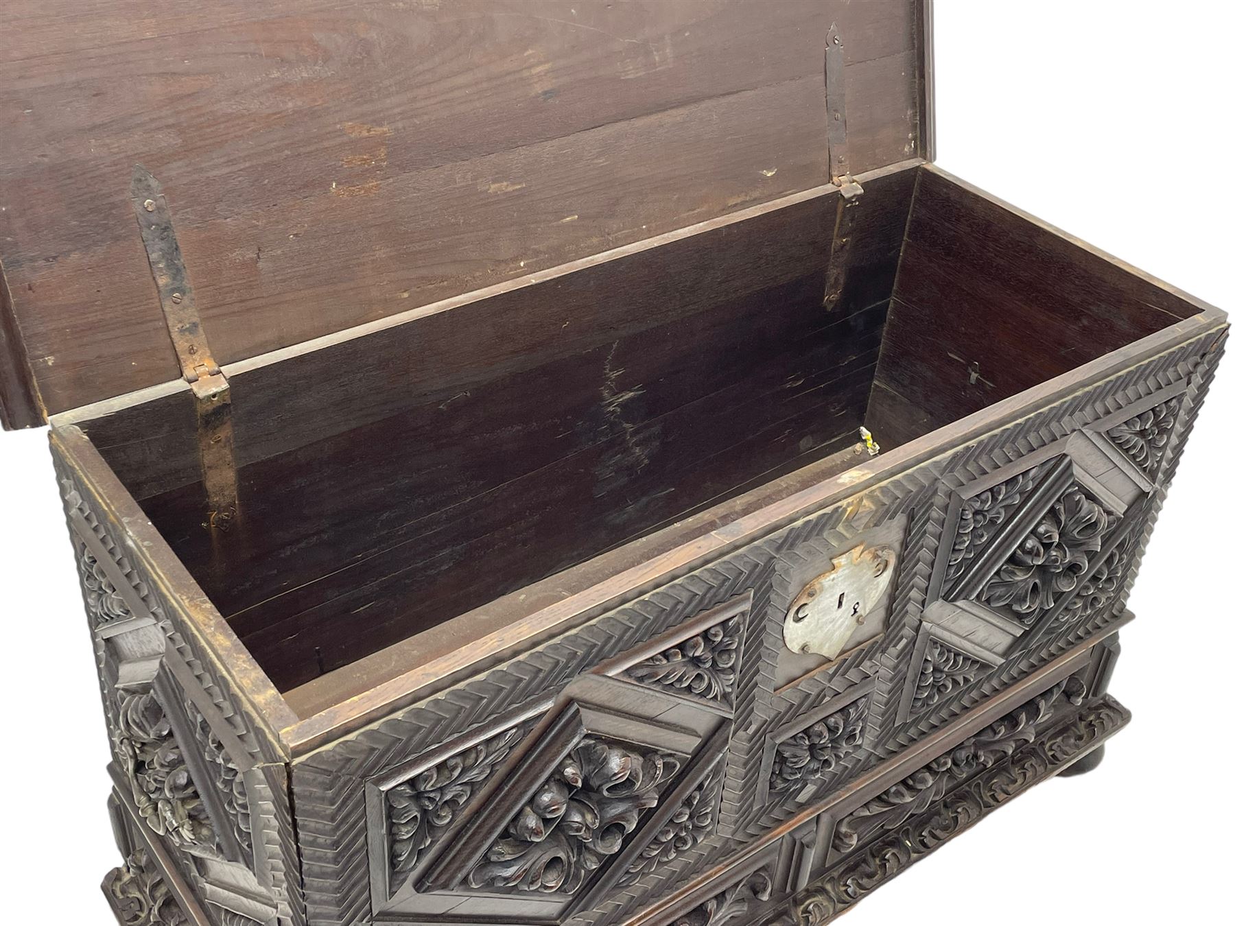 Early 20th century carved hardwood kist or mule chest of small proportions, moulded rectangular hinged lid over foliage carved geometric lozenge panels, the frame carved with chevron banding, fitted with two drawers, the drawer fronts carved with extending leaf motifs over a foliage carved lower moulding, on turned feet