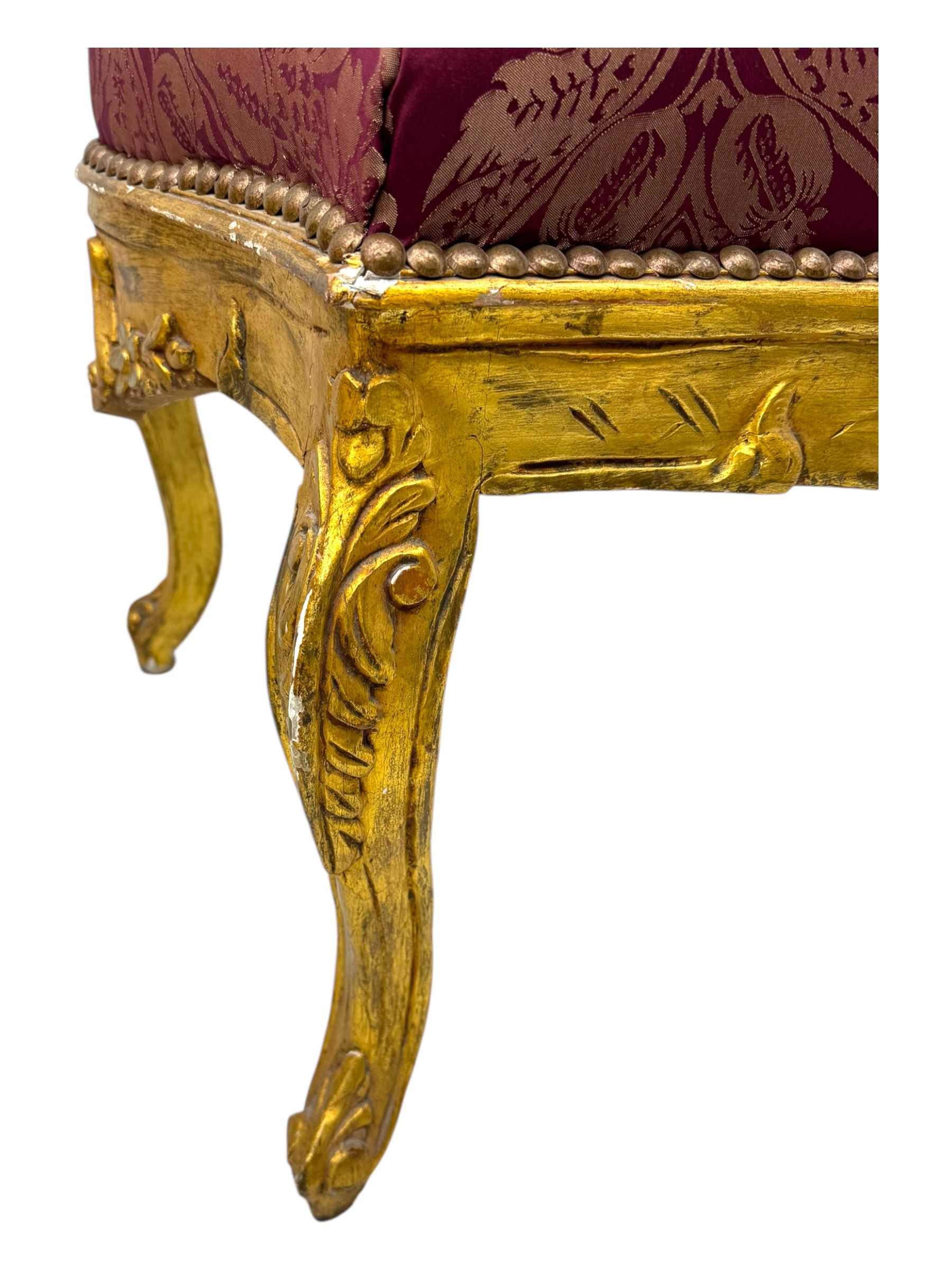 Pair of Louis XV-design giltwood stools, each upholstered in red damask fabric with slight variations in patterns, the carved frames adorned with scrolling foliage and shell motifs, raised on cabriole supports