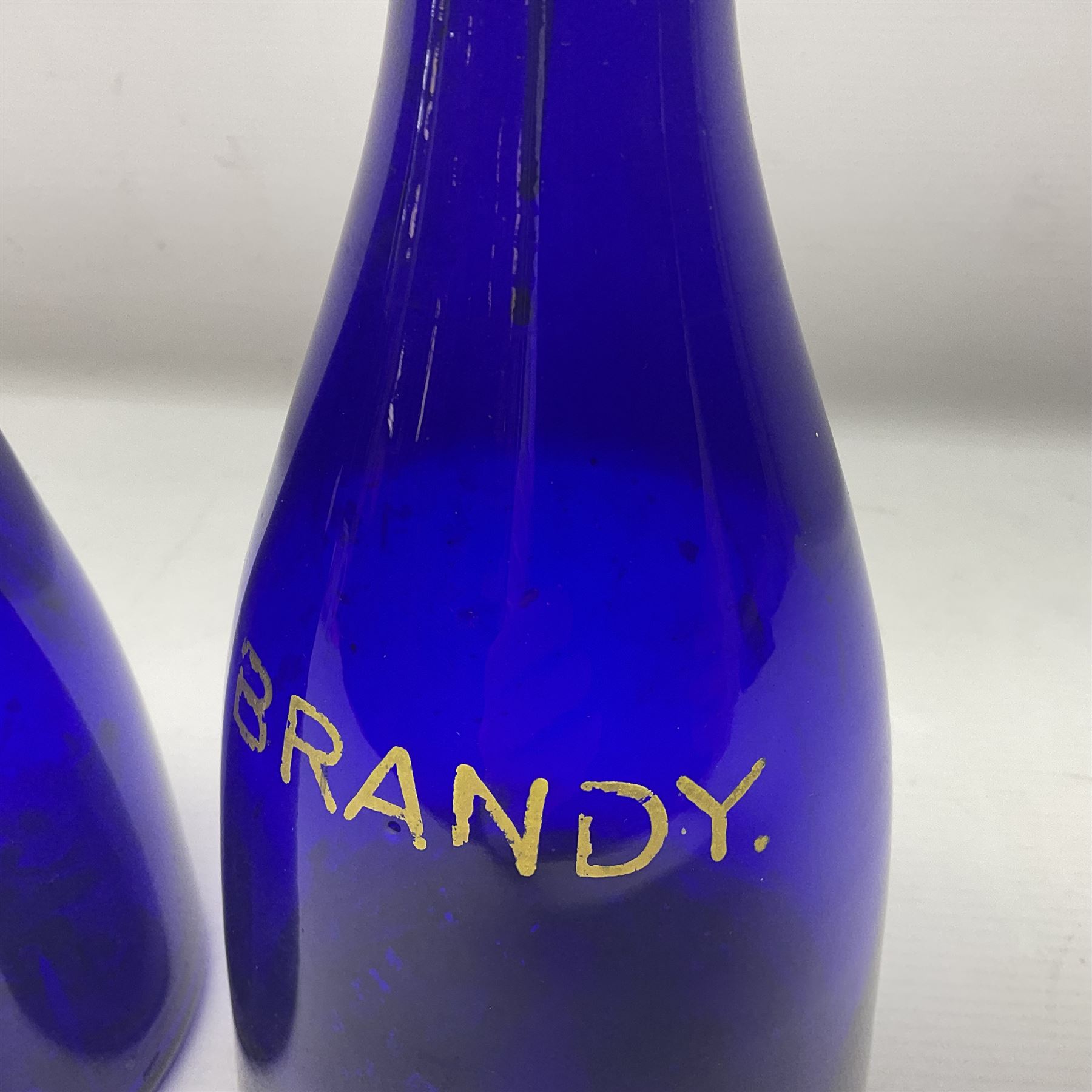 Pair of early 19th century blue glass decanters with teardrop stoppers, with gilt writing, the first marked Gin the second Brandy 