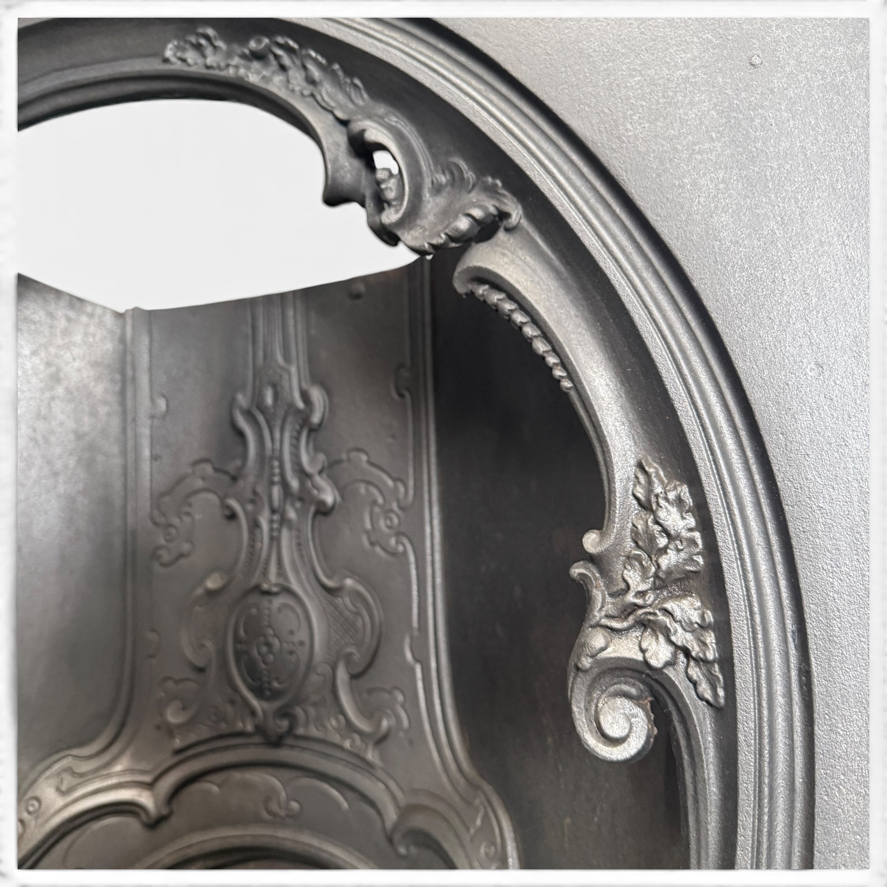 Victorian cast iron fireplace, the arched surround cast with scrolling foliate ornament and central shield-shaped cartouche, fitted with a bowed fire basket, in black painted finish