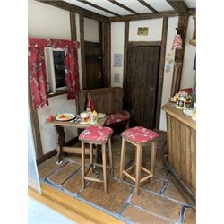 Dolls house scale room setting of a public house bar with tiled floor and beam and plaster ceiling and walls, bench seat, stools and table set out with a meal and drinks, large planked finish canted bar well stocked with food, drinks, bottles, glasses etc and bartender figure behind; electrically illuminated with sliding perspex access panel to front W38cm D28cm H24cm