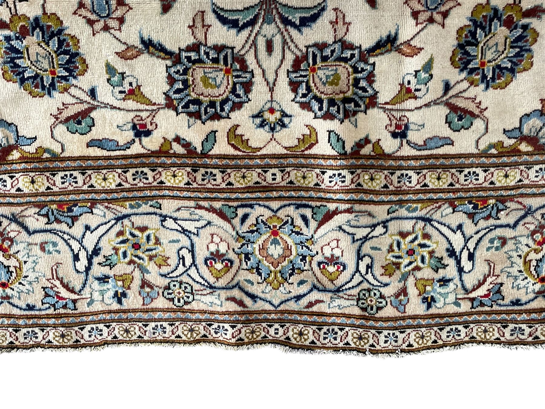 Persian Kashan ivory ground carpet, the field decorated with scrolling branches with foliate and palmette motifs, repeating border with stylised plant motifs, within floral and geometric pattern guard stripes 