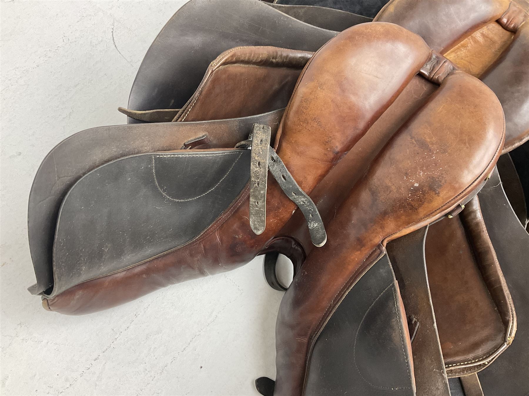 Collection of nine saddles, mainly havana leather to include a racing saddle and a Goodwin saddle, some with stirrups and leathers 