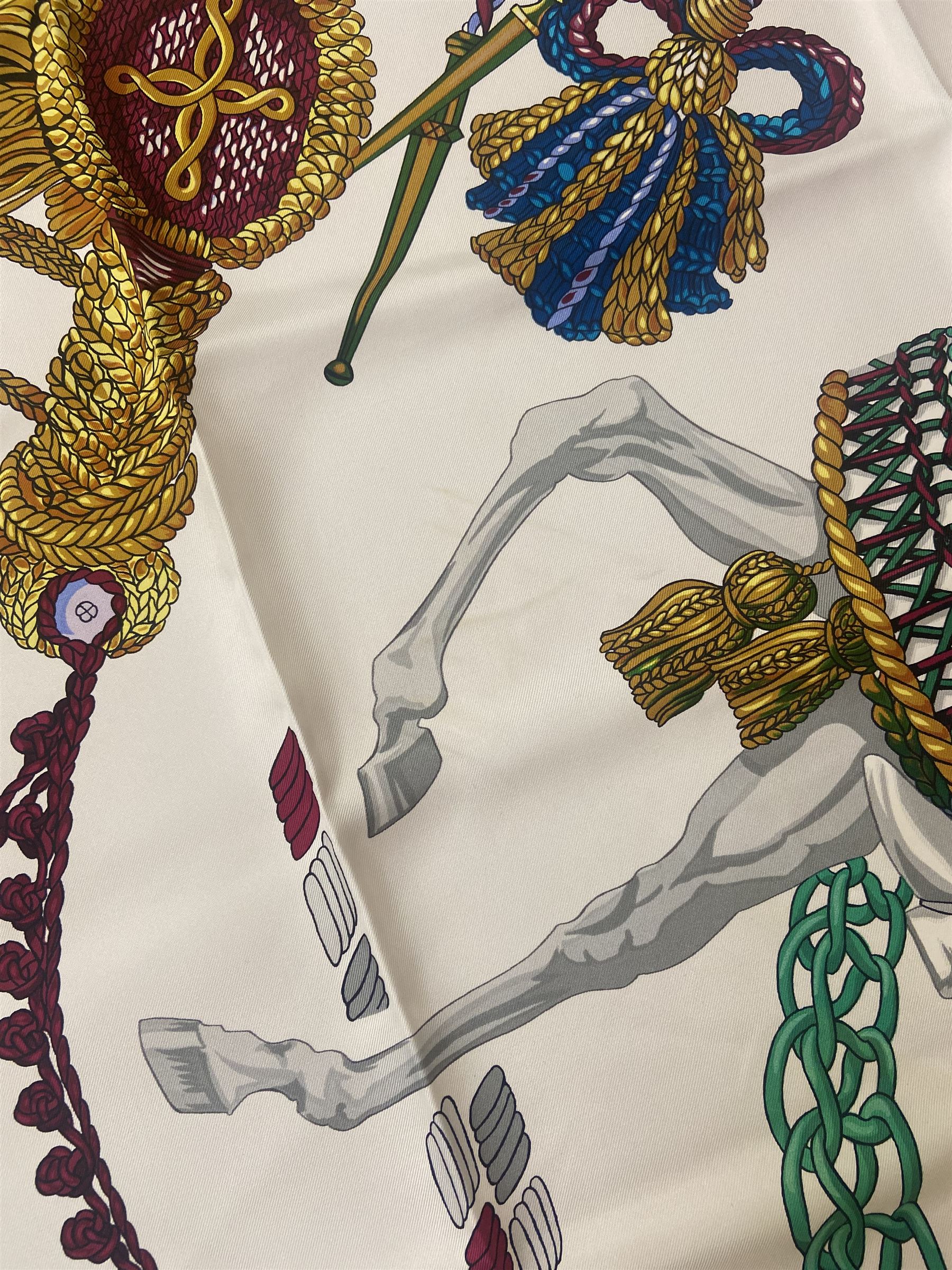 Hermès 'Le Timbalier' silk scarf, designed by Francoise Heron in 1961, printed with a central image of a gentleman on horseback donning extravagant dress, on white ground surrounded with colourful stylised knotted ropes, contained within peacock blue border, with rolled hand stitched edges and Hermes material label, 87cm square