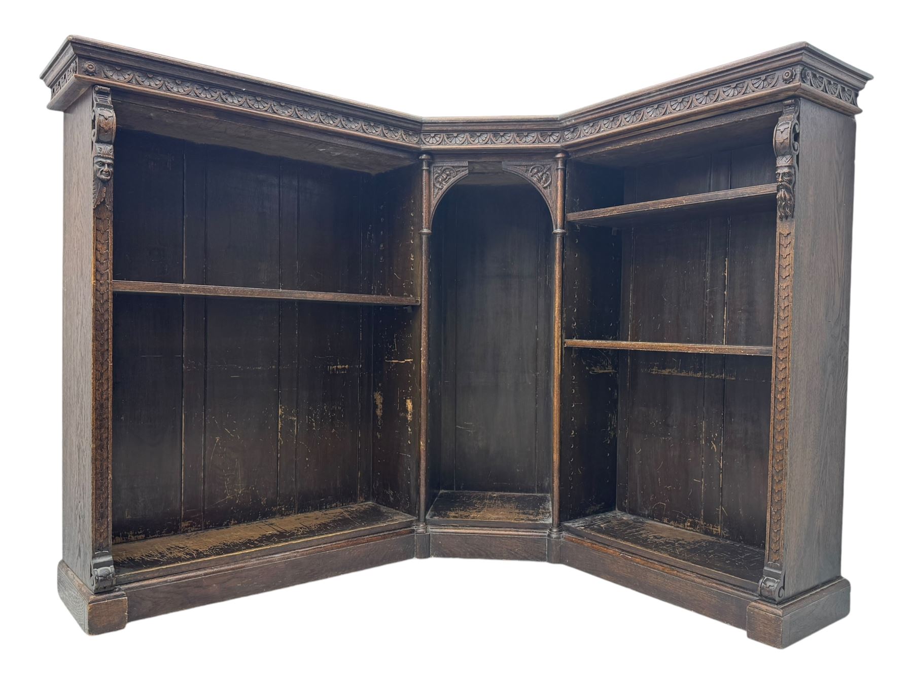 Victorian carved oak corner bookcase, L-shaped form, moulded top over lunette carved frieze, decorated with S-scroll and mask carved corbels with trailing acanthus leaves, fitted with adjustable shelves, on moulded plinth base 