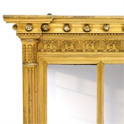 Regency period gilt and gesso framed tripartite overmantel mirror, projecting cavetto cornice applied with globular mounts, the frieze carved with repeating scallop and floral urn motifs, flanked by canted cluster-column pilasters with acanthi capitals, the triple rectangular bevelled plates within reeded slips, on skirted ebonised base
