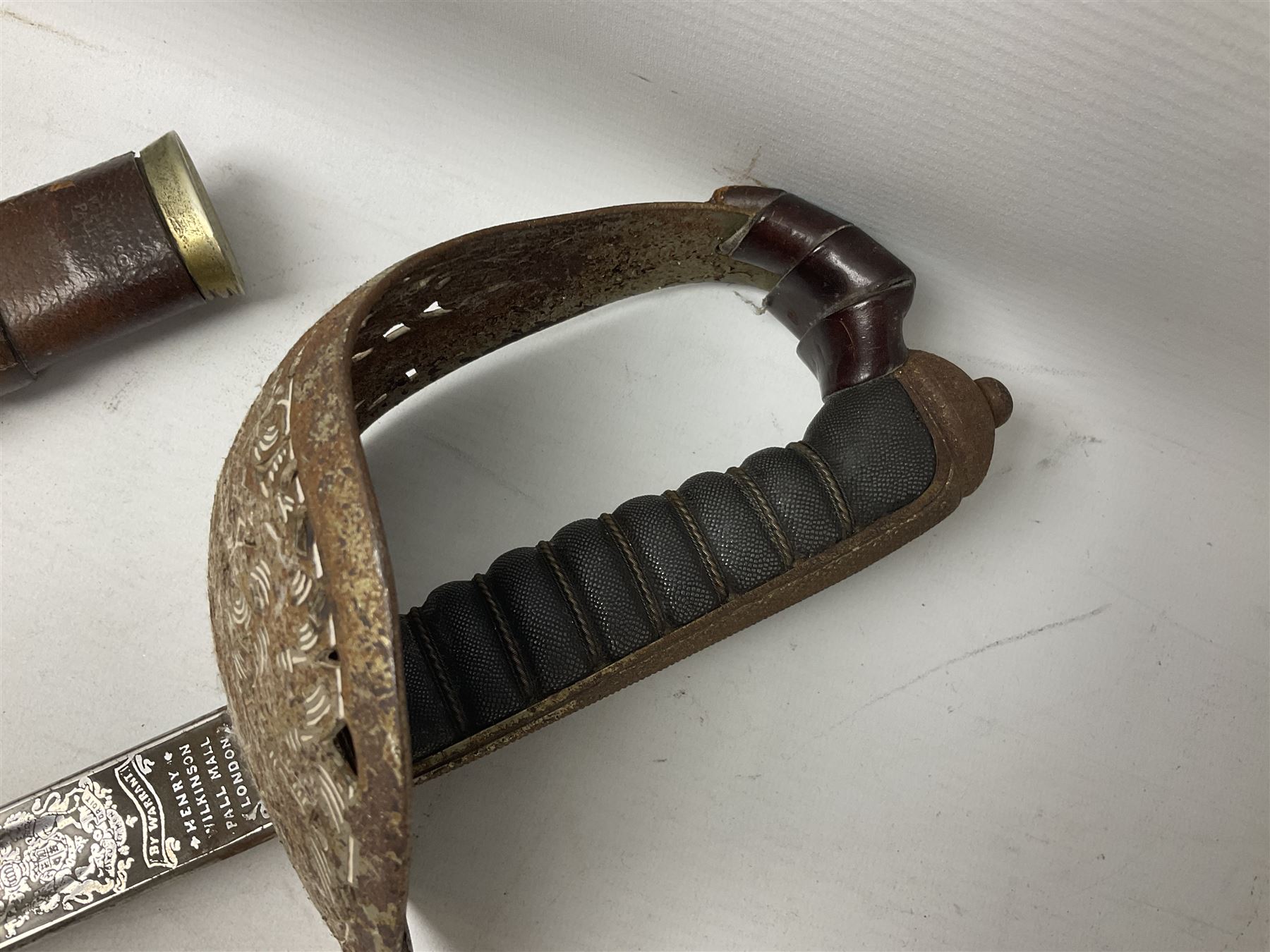 George V 1897 pattern Army Officer's sword by Henry Wilkinson Pall Mall London, the 82.5cm 'London Made' blade etched to both sides with Royal Crests and cyphers etc, pierced half-basket hilt with wire-bound fish skin grip and remains of leather knot strap; in leather covered field service scabbard L101cm overall; and two 14th Prince of Wales Own swagger sticks (3)