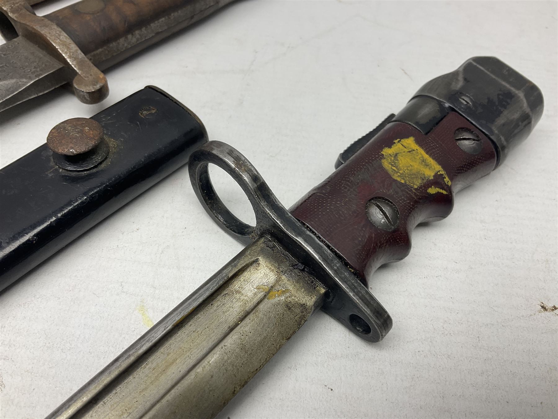 British No 7 MKI knife bayonet with 20cm single edged fullered clipped point blade;  blackened steel, large muzzle ring cross-guard; blackened swivelling pommel marked 'F5H'; red Tufnol composite grips; in blackened steel scabbard L33cm overall; British Pattern 1888 bayonet with scabbard; and German Ersatz bayonet with scabbard (3)