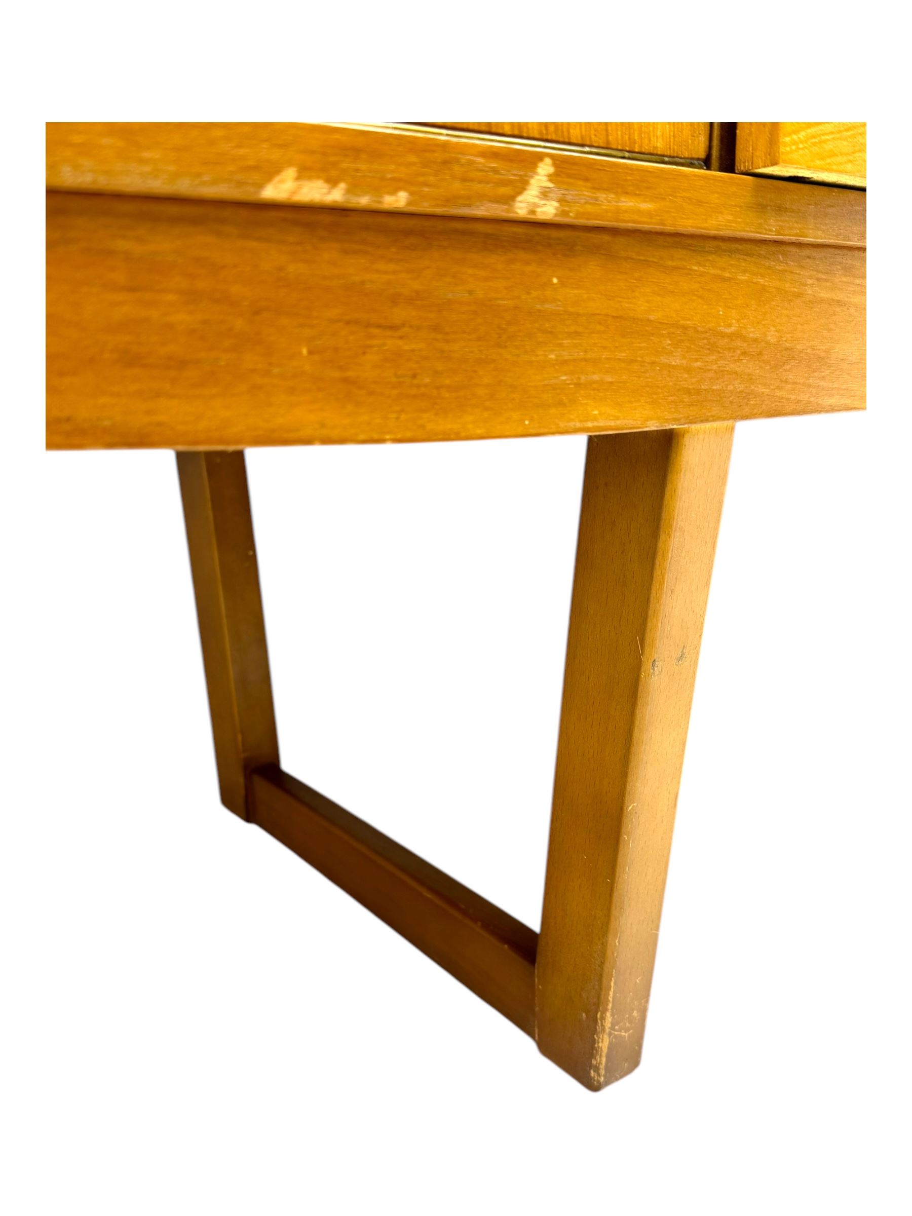 Mid-20th century teak sideboard, fitted with a fall-front cupboard, three drawers including a green baize-lined cutlery drawer, and a double cupboard, with integrated handles, on sleigh supports