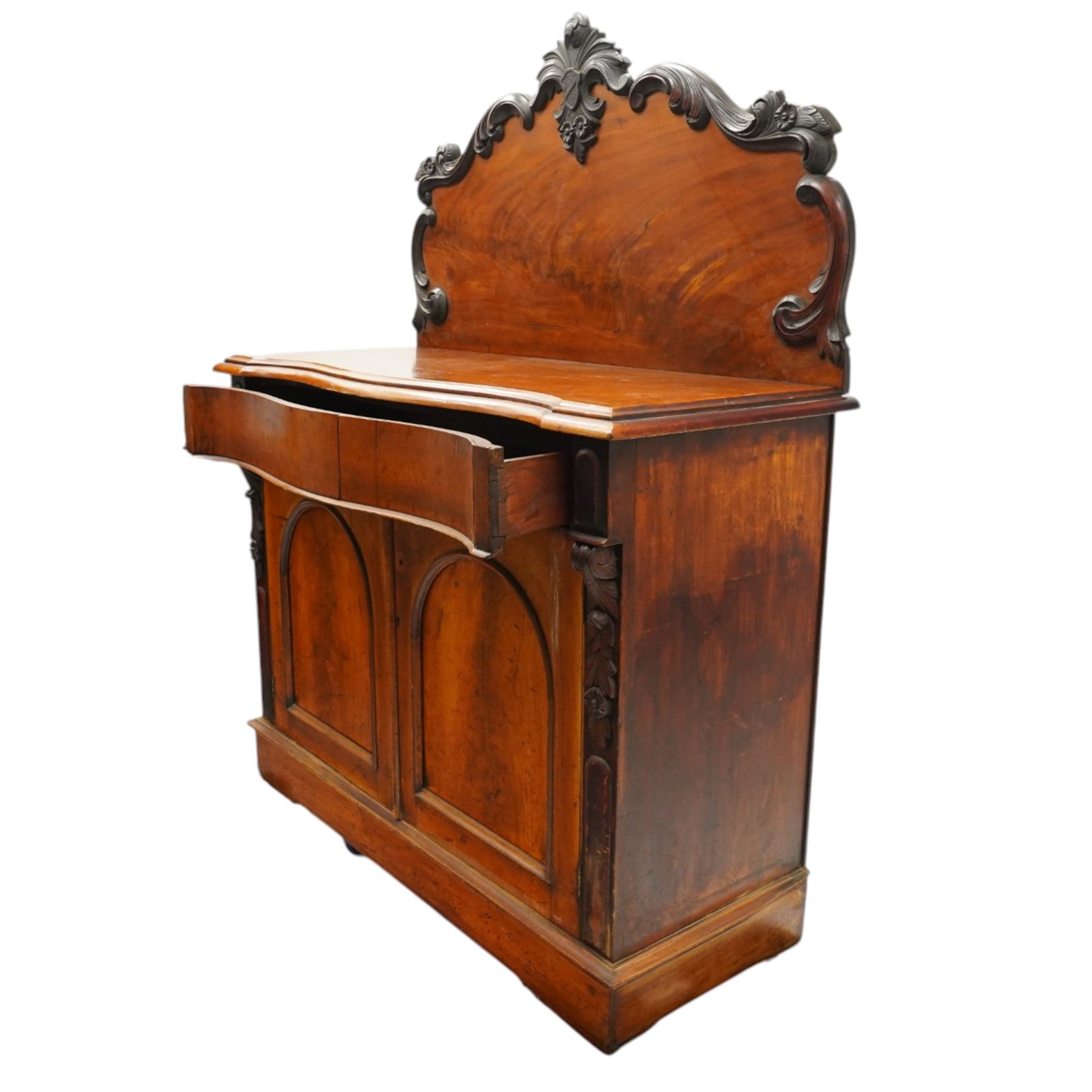 Victorian mahogany chiffonier, raised back with applied carvings, above a serpentine fronted base, a single frieze drawer, above a cupboard with shelf and drawer with campaign handle, raised on a plinth base