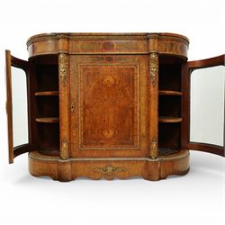 Late Victorian figured walnut credenza, the shaped demi-lune top with cross-banding and stringing over an inlaid frieze with foliate gilt-metal mounts, fitted with a central geometric-inlaid panelled door, flanked by convex-glazed side-cabinets with a gilt metal slip and outer-banding, the uprights surmounted by gilt-metal cartouche mounts with cascading foliage details, raised on a shaped skirted base with central female-mask gilt mount