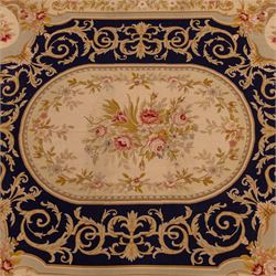 20th-century Aubusson-style woven tapestry wall hanging of rectangular form, the design with a central oval floral medallion composed of delicate sprays in soft pinks, creams, and muted green enclosed by an elaborate dark blue scrolling acanthus ground enriched with foliate ornamentation, field framed by floral cartouches to the corners and multiple guard borders in pale blue, ivory, and ochre tones