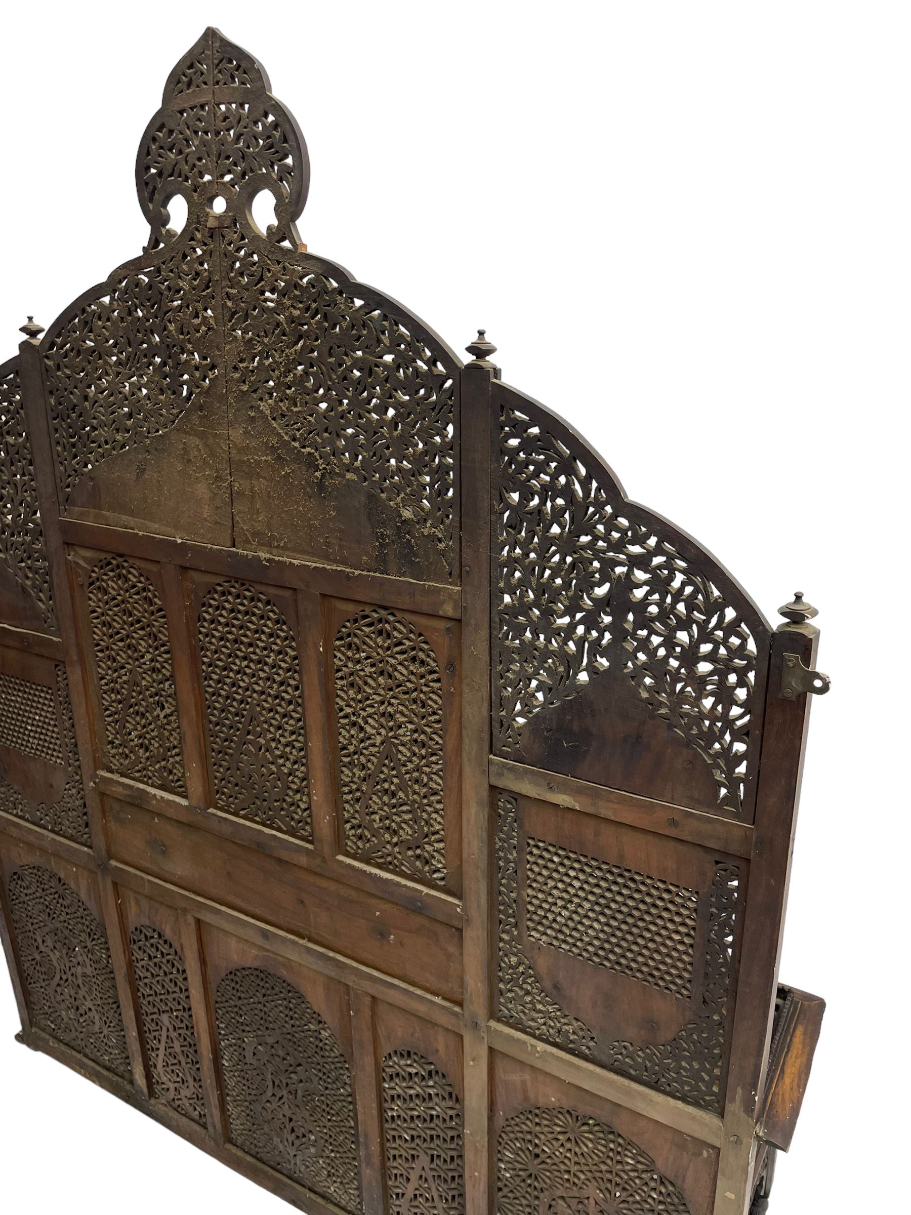Late 19th century Indian Burmese carved and pierced hardwood and brass inlaid wall shelf, the shaped back profusely decorated with trailing and interlaced foliage, with projecting architectural structures, the central balcony with canopy top and five open windows with arched apertures on columns, two flanking five-sided balconies, the shelf supported by six foliate carved columns with pierced cusped pointed arches 