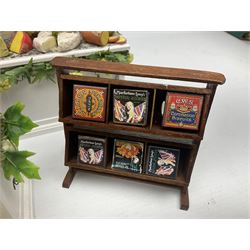 Collection of miniature dolls house grocery shop furniture and produce, comprising glazed corner counter with brass style cash register, shelved preserves unit, pies, cheese board and trays of meats, pair of white cheese counters, biscuit display with six tins, glazed preserves cabinet, pair of shop chairs and four further cheese boards complete with grapes and label flags