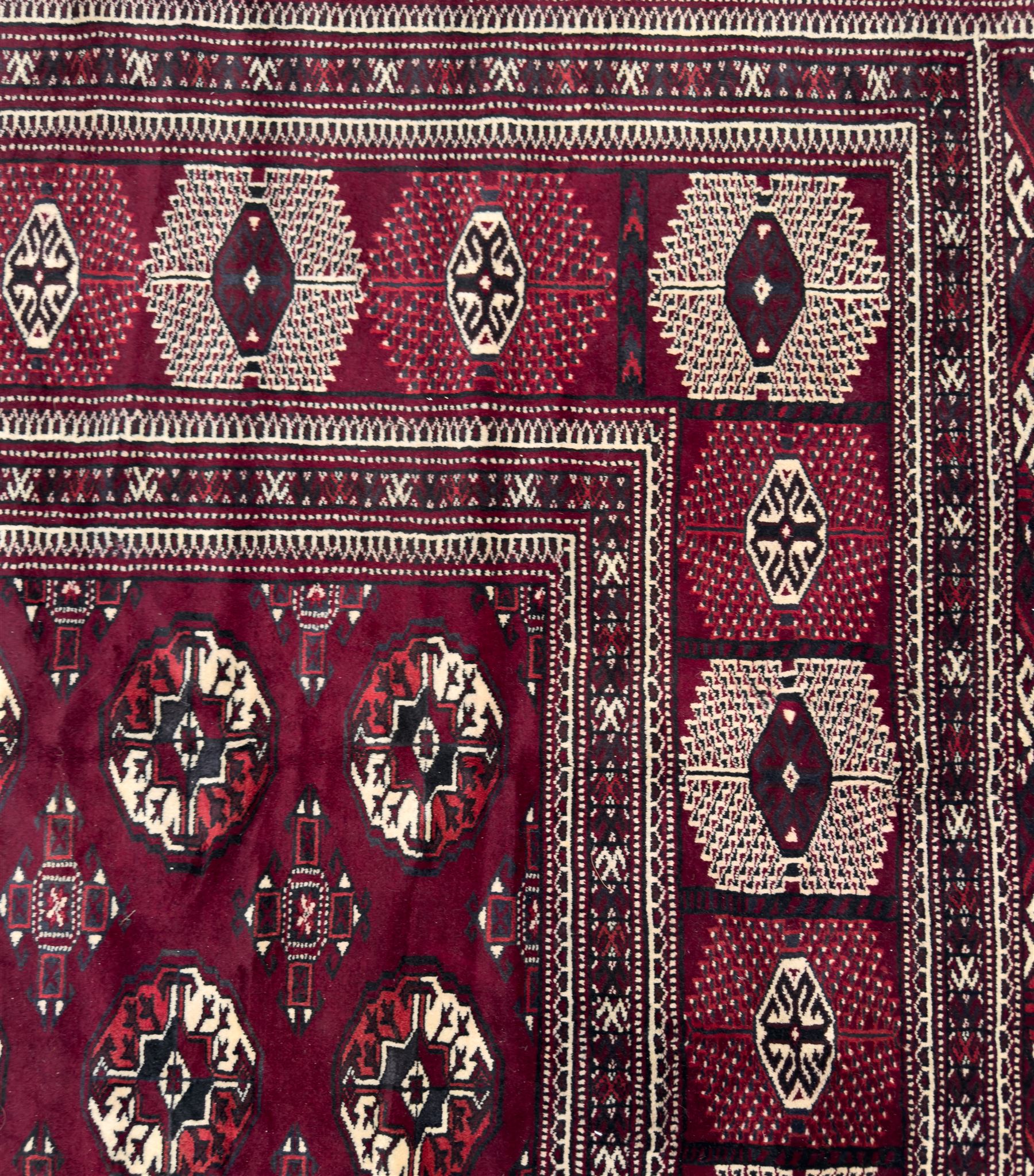 Northeastern Persian Yamut  hand-knotted carpet, the rich burgundy field with repeating rows of stepped gul motifs in cream and black, enclosed by multiple linear and geometric borders with hooked motifs and diamond medallions