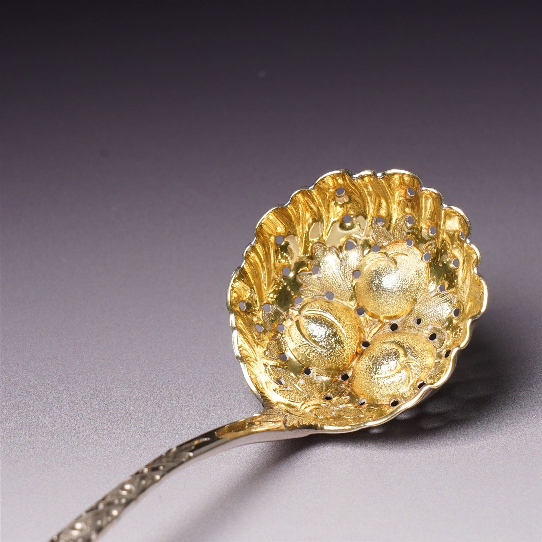 George III silver 'berry' spoon with later embossed and gilded bowl and engraved stem London 1786, sifting spoon similarly gilded and decorated and a George III silver fiddle and thread pattern table spoon London 1810 (3)
